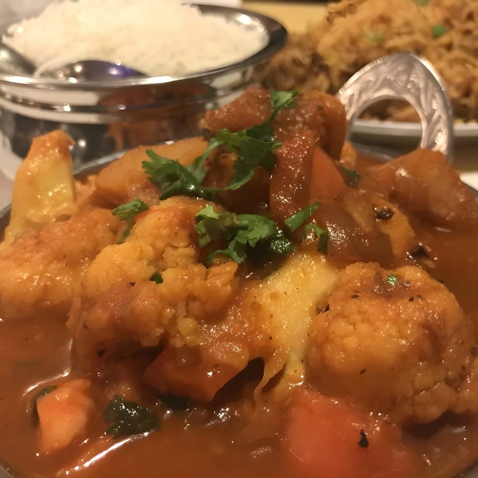 Close-up of Indian Aloo Gobi with cauliflower and potatoes, garnished with cilantro, served with rice.